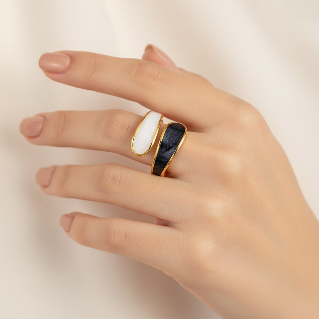 Hand wearing a 18k gold plated white and black band ring on a beige background