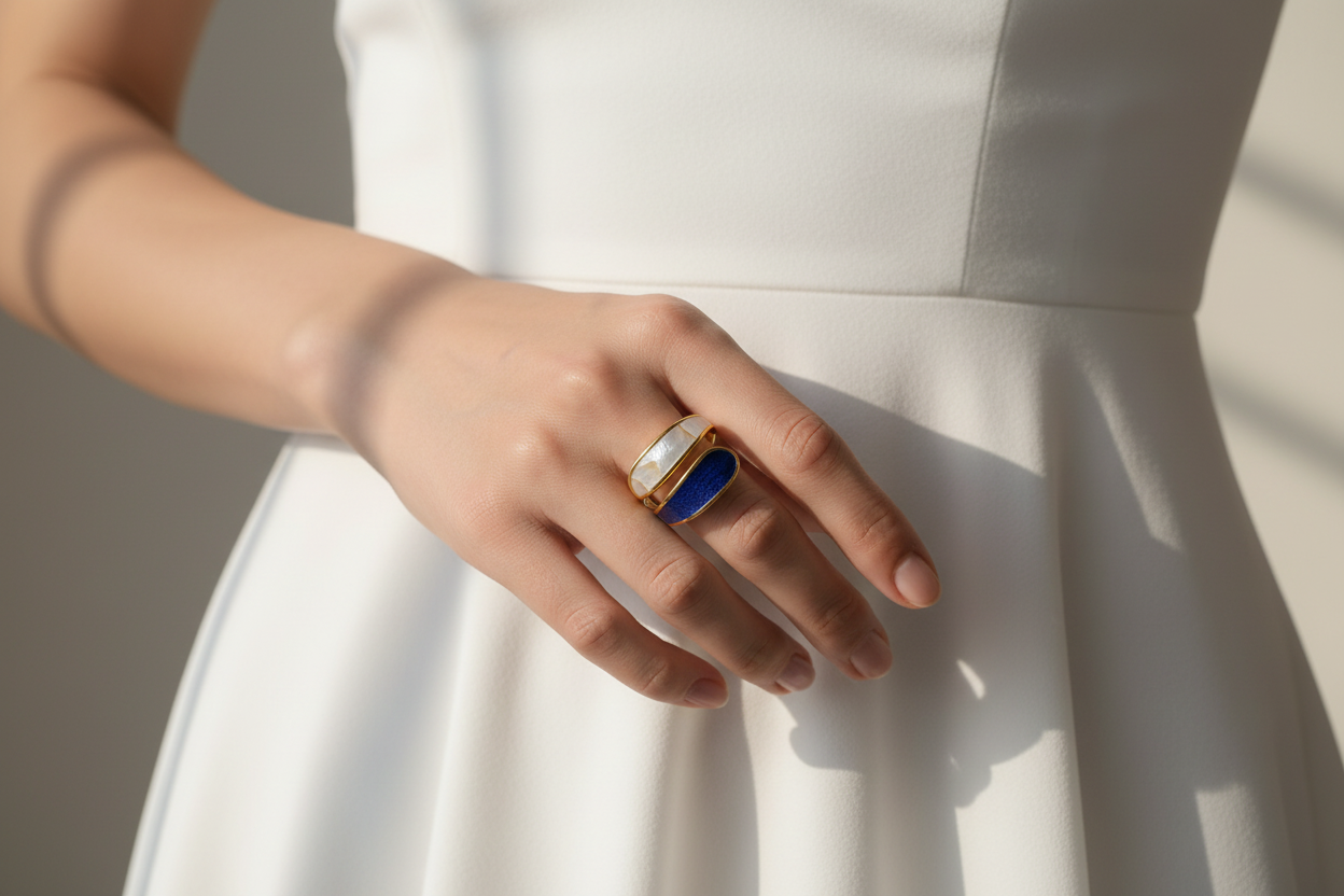 Hand wearing a 18k gold plated ring with white and black stone on a white background