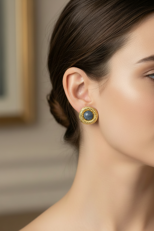 Close-up of a woman wearing gold earrings with a dark stone.