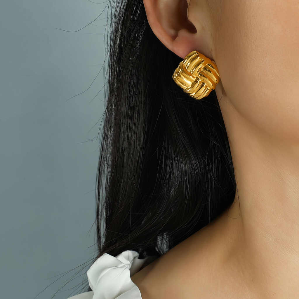 Gold earrings worn by a person with a neutral background