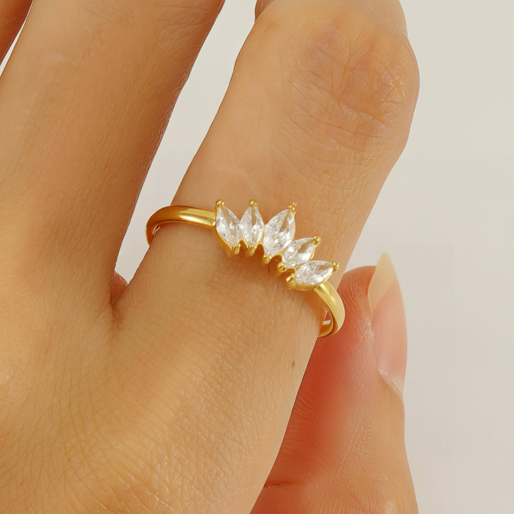 Gold ring with clear gemstones on a person's finger against a neutral background