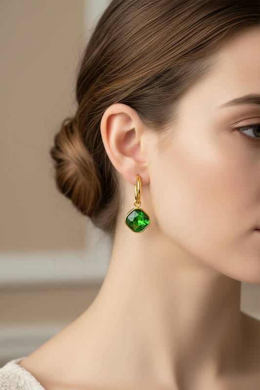 Close-up of a person wearing a green gemstone earring with gold detailing.