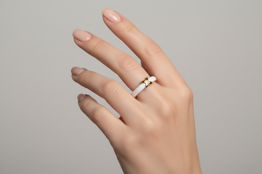 Hand wearing a white 18k gold plated ring on a gray background