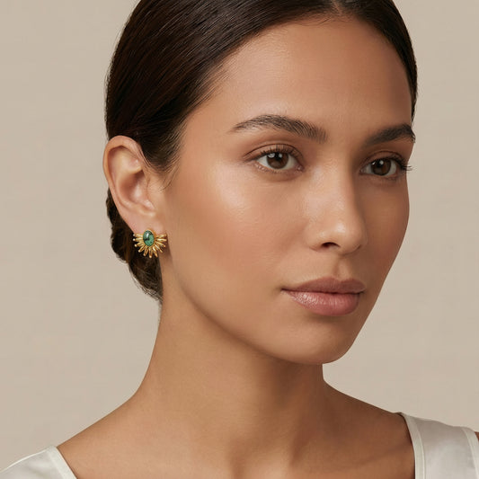 Woman wearing a gold earring with a green gemstone on a beige background