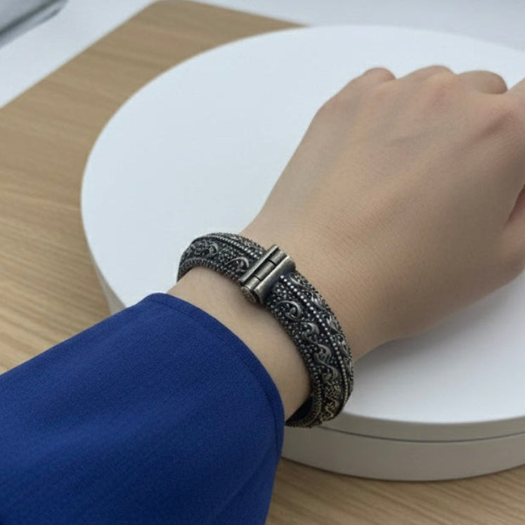 Hand wearing a bracelet on a white surface with a blue sleeve