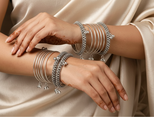 Close-up of hands wearing multiple silver bangles on a green fabric background