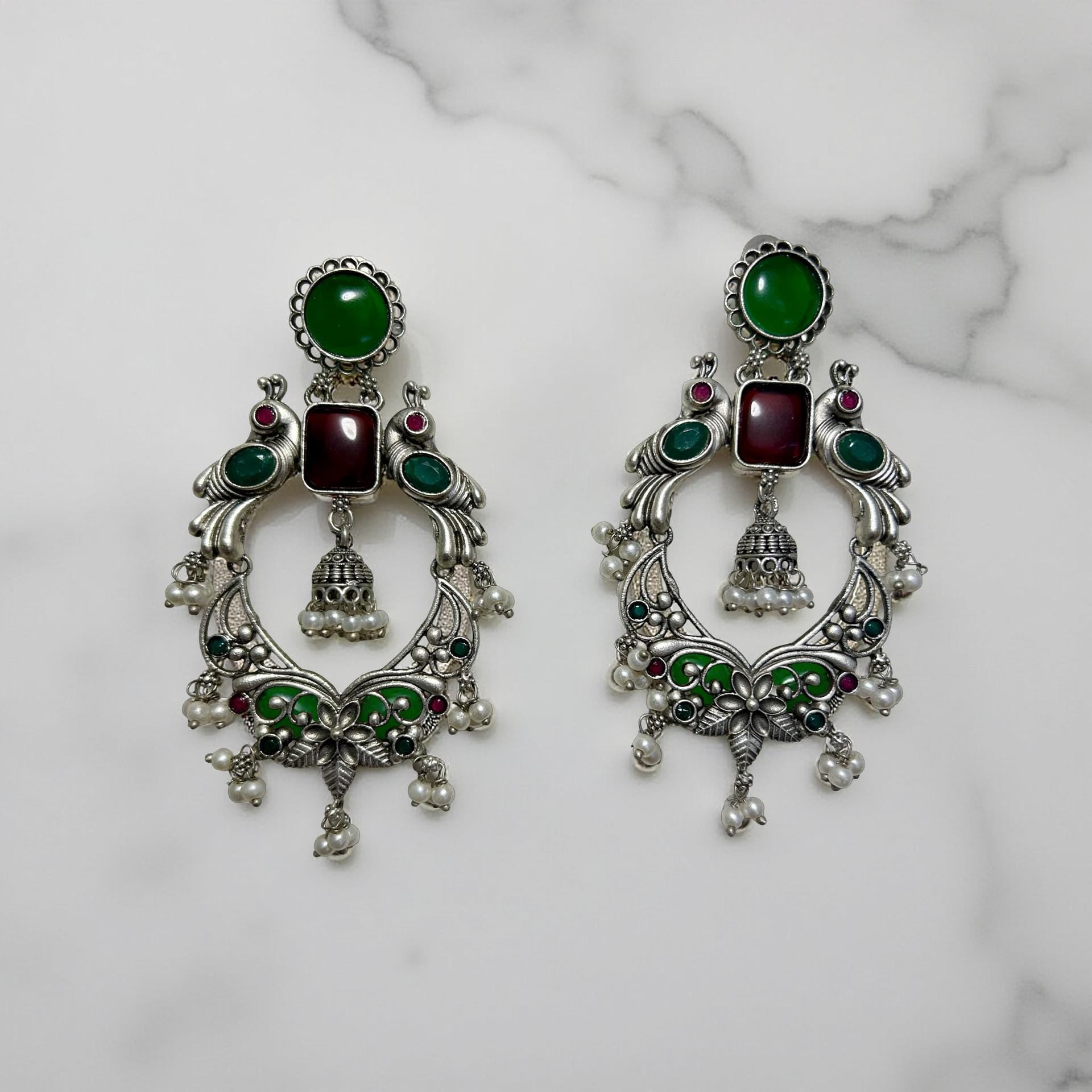 Pair of ornate earrings with green and red stones on a marble background