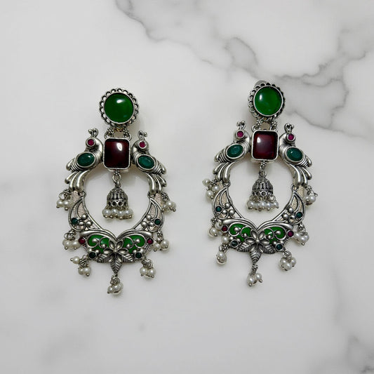 Pair of ornate earrings with green and red stones on a marble background