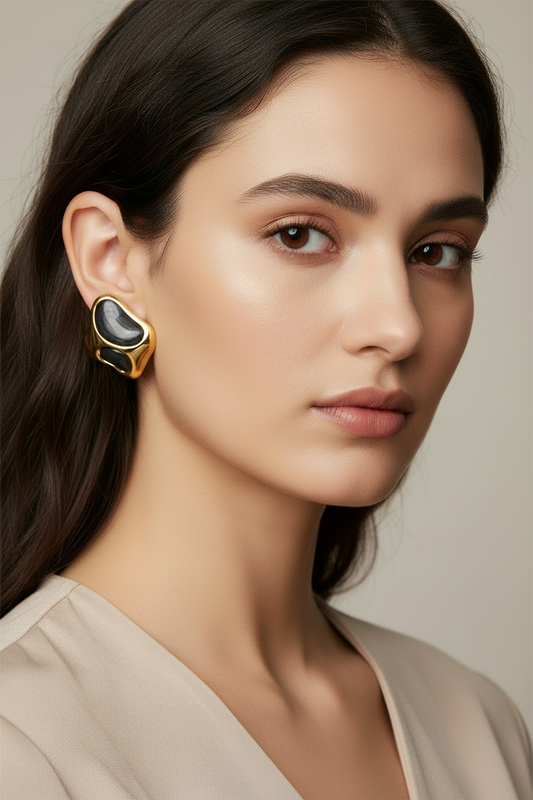 Woman wearing a gold earring with a black stone on a neutral background