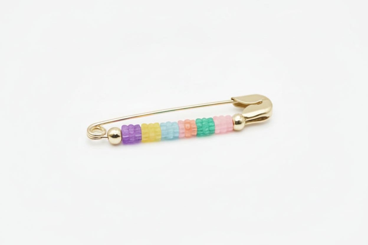 Metal safety pin with colorful beads on a light gray background
