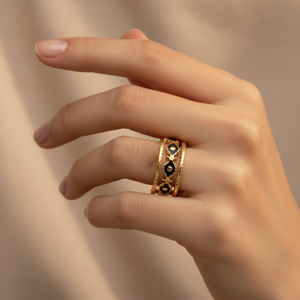 Hand wearing multiple gold rings with intricate designs on a neutral background