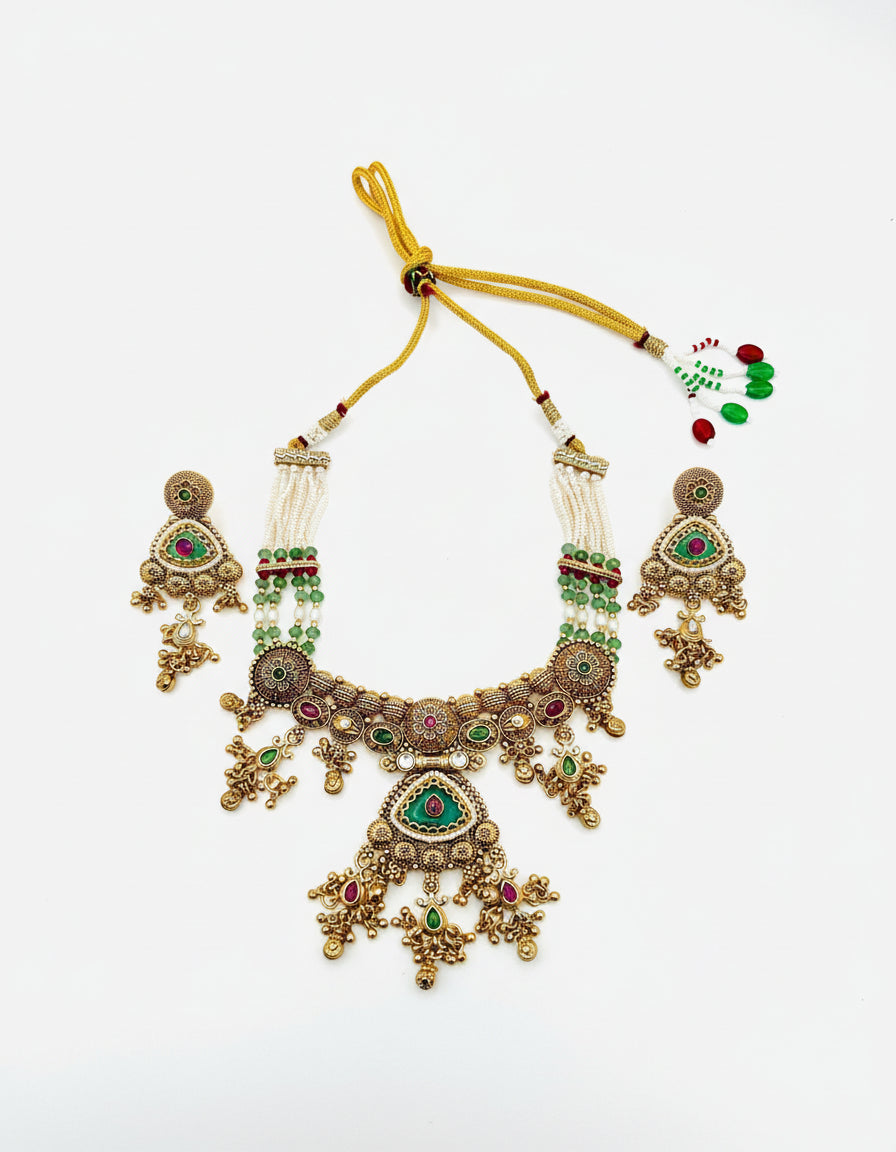 Ornate gold necklace with green and red stones on a white background