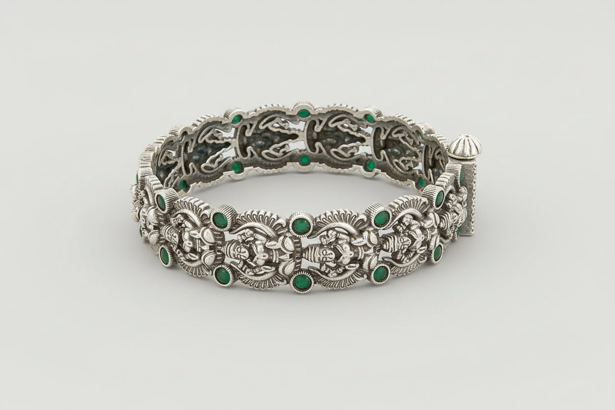 Decorative Oxidized silver bracelet kada with green gemstones on a wooden surface