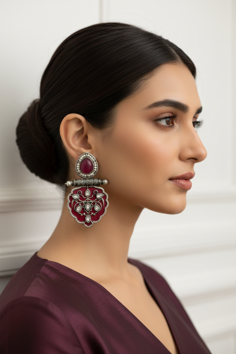 Woman wearing a large, ornate earring with a red gemstone against a neutral background