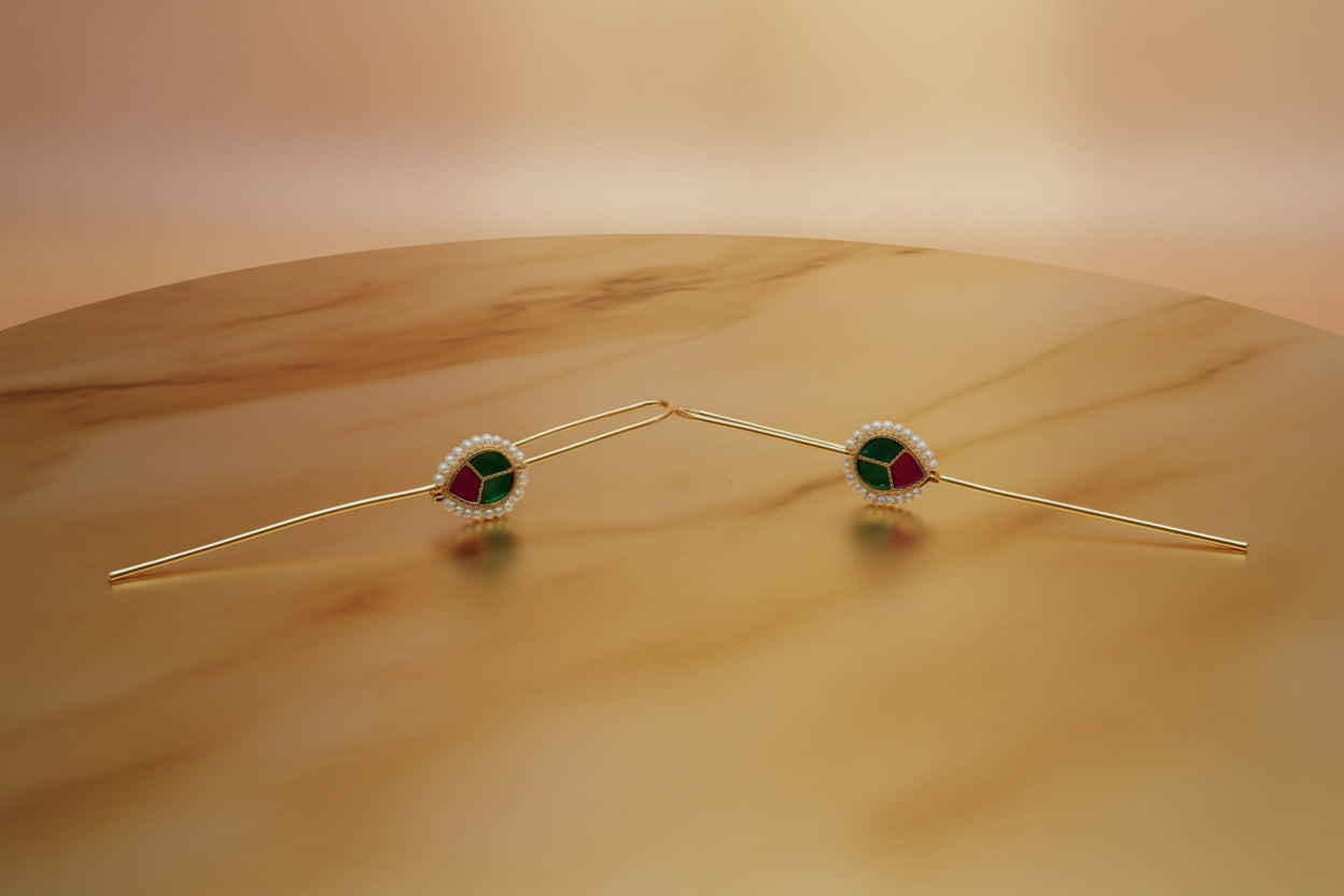 Two gold tone needle ear cuff earrings with greenish gemstones on a white background