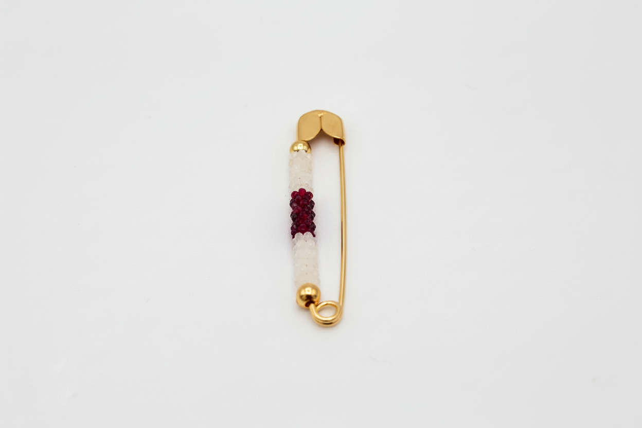 Gold safety pin with red beads on a white background