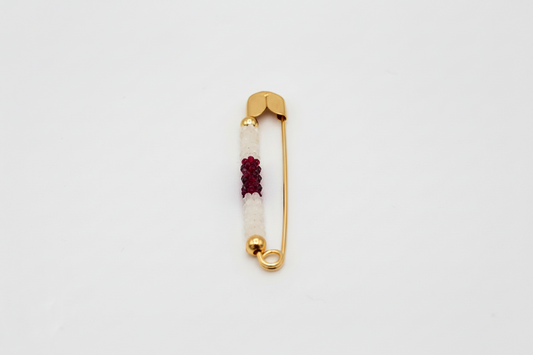 Gold safety pin with red beads on a white background