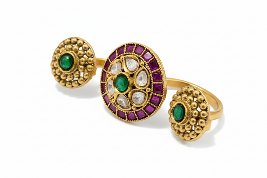 Gold ring with green and red gemstones on a pink background
