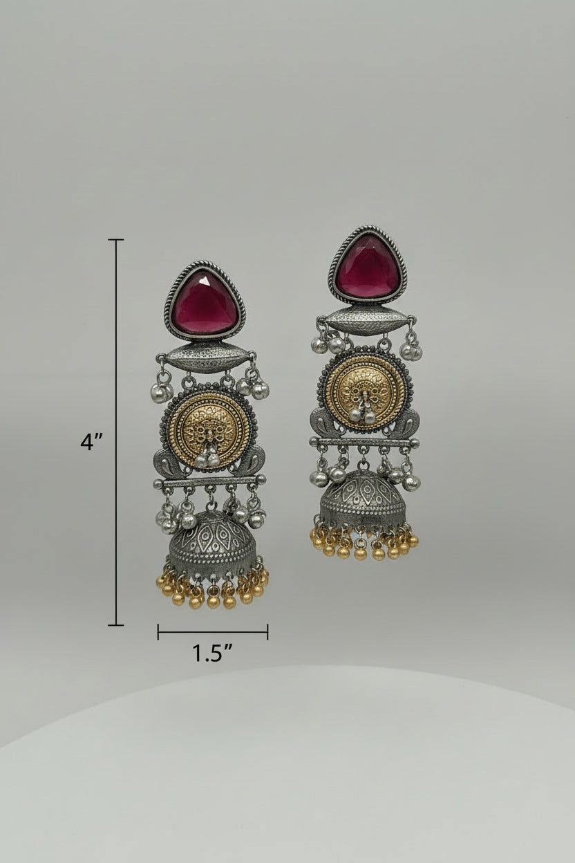 Pair of ornate earrings with red gemstones on a gray background