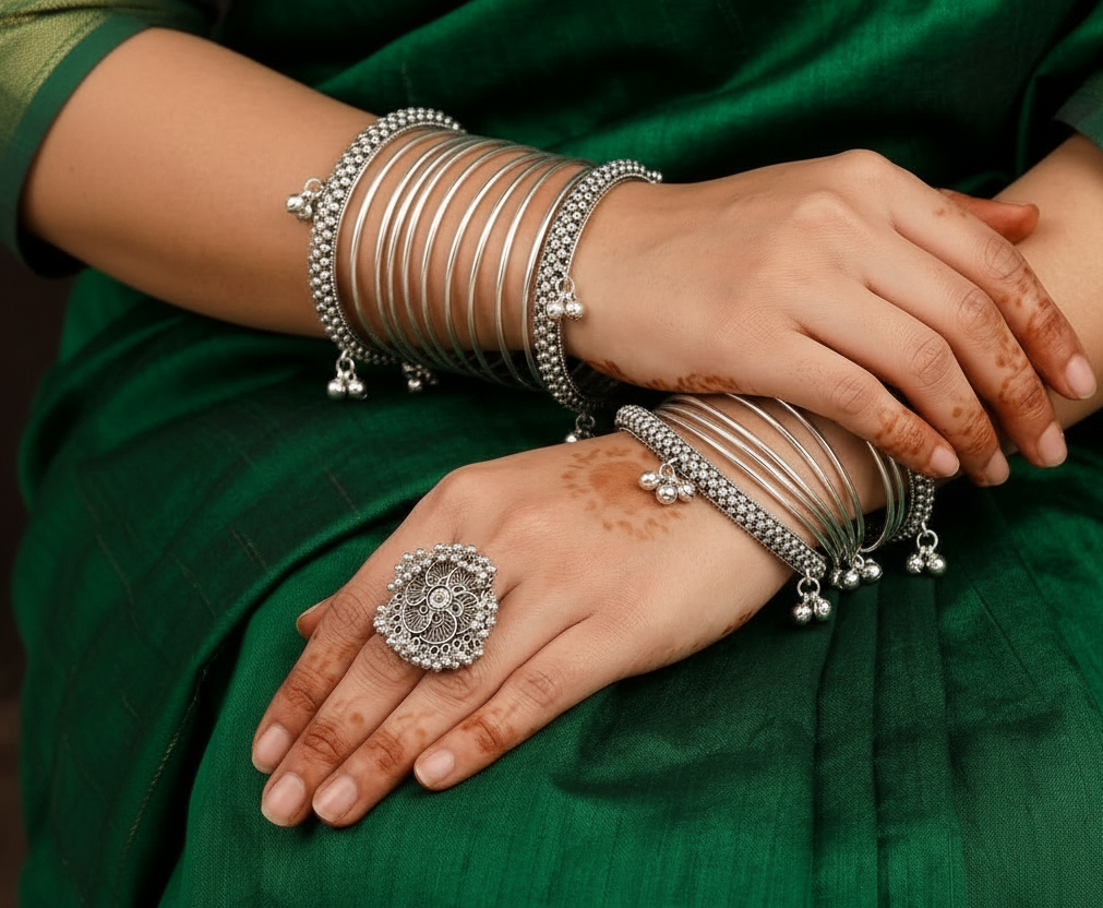 Silver jewelry including bangles and rings on a person's hands with a green fabric background.