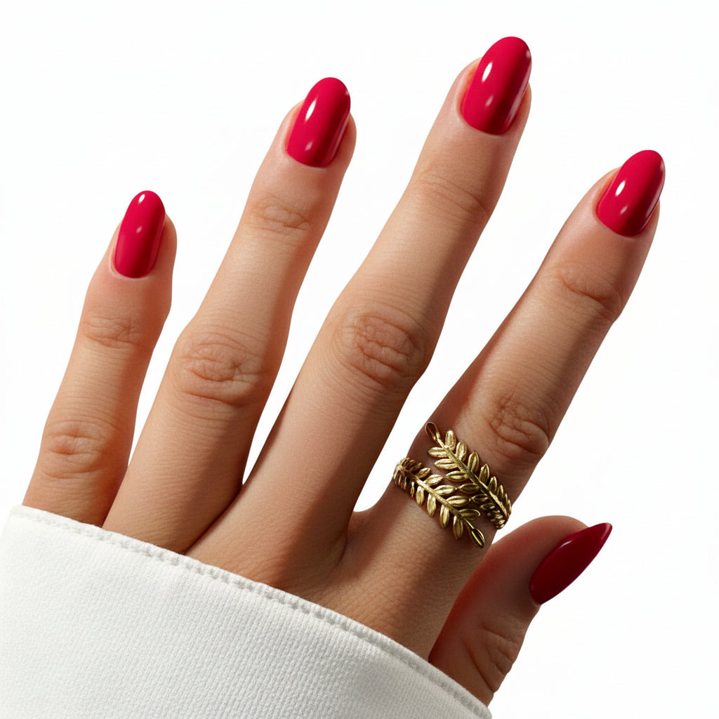 Hand with bright pink nails and a gold leaf ring on a white background