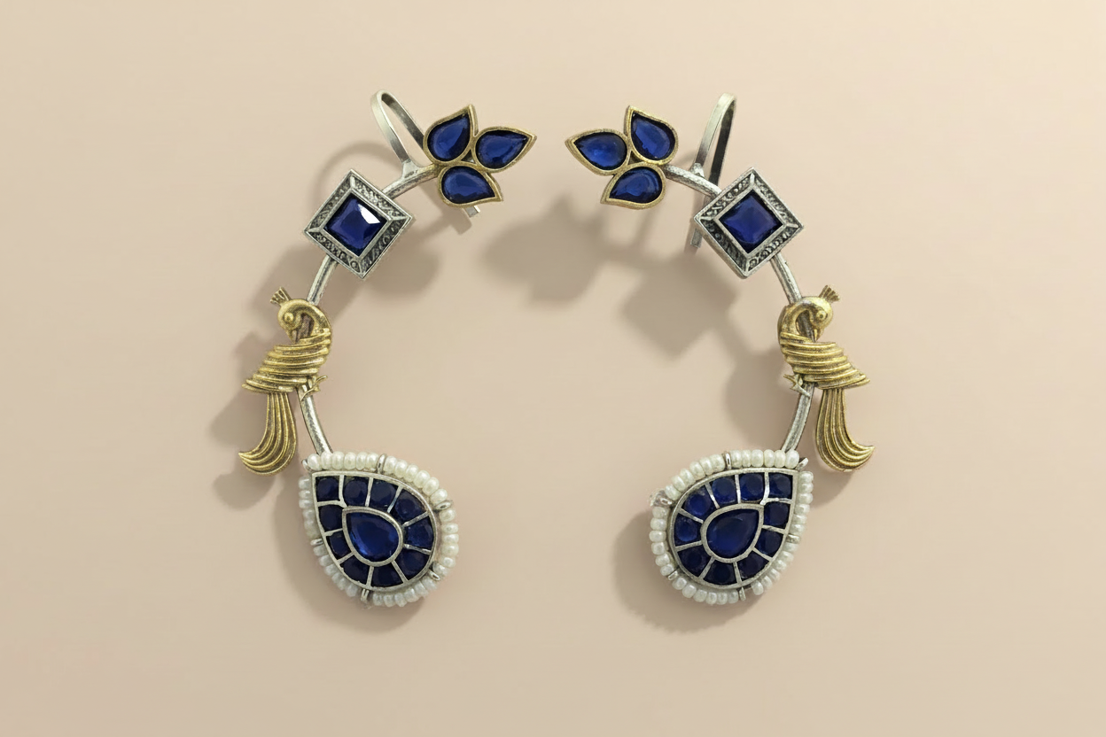 Pair of cuff earrings with blue stones and gold accents on a beige background
