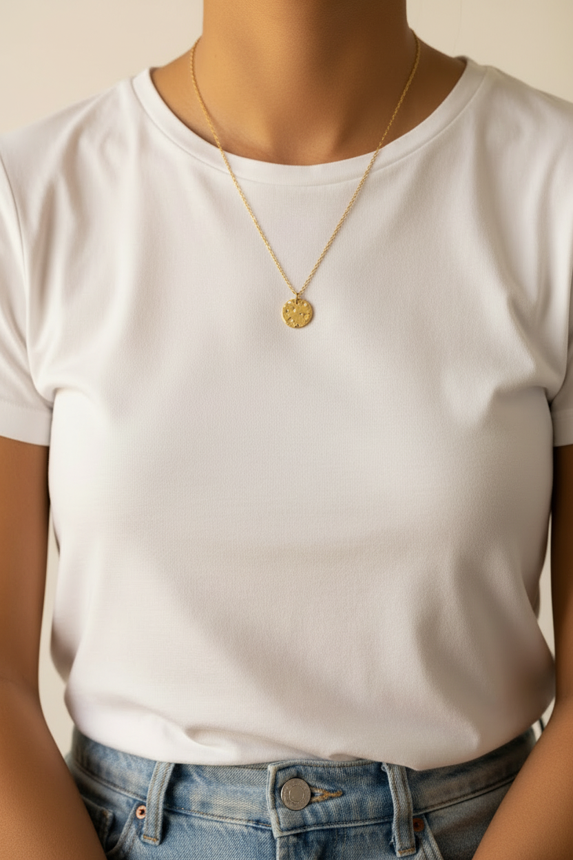 Person wearing a white t-shirt and blue jeans with a gold necklace featuring a circular pendant.