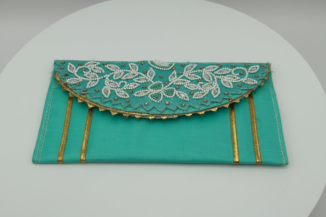 Turquoise clutch with gold accents and intricate white embroidery on a light gray background