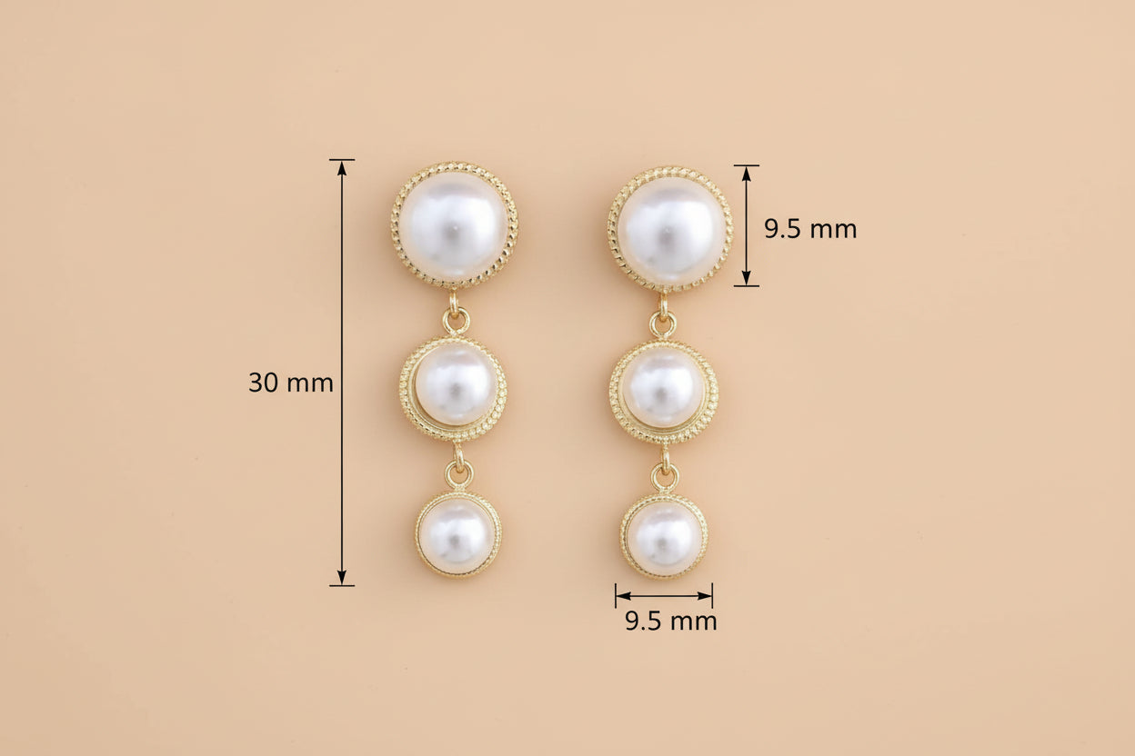 Pair of pearl earrings with gold accents on a #FFE5B4 background 