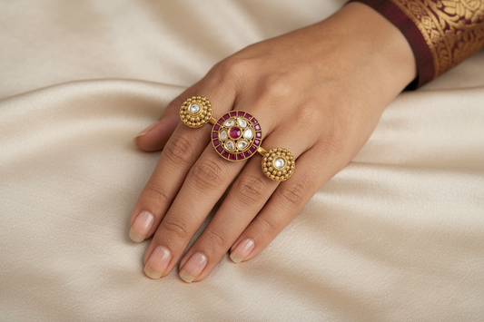 Hand wearing gold rings with gemstones, next to a box and more gemstones on a dark surface.