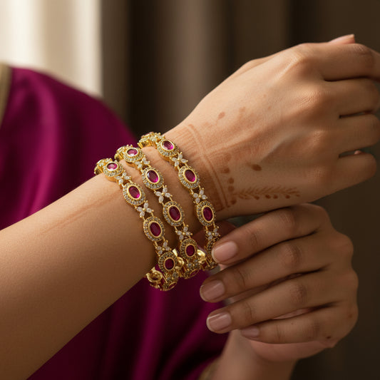 Gold bracelets with red stones on a pink background