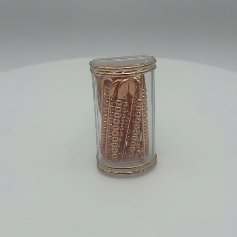 Small cylindrical metallic safty pins with embossed design on a white background