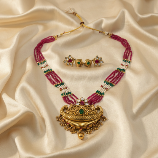 Ornate gold necklace with pink beads and green gemstones on a beige fabric background