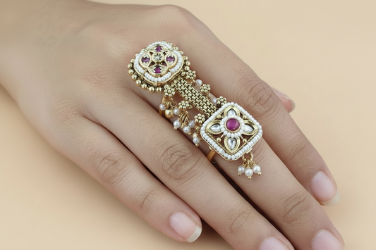 Gold and pearl single finger long ring with red gemstones on a hand against a pink fabric background