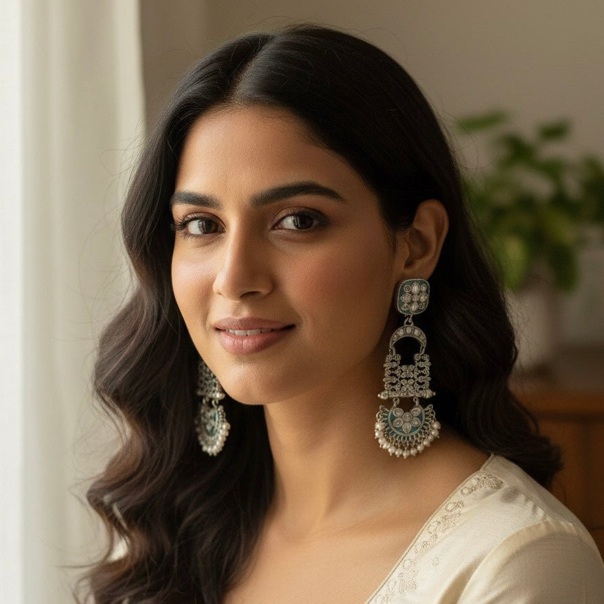 Woman wearing large, ornate earrings indoors with a neutral background