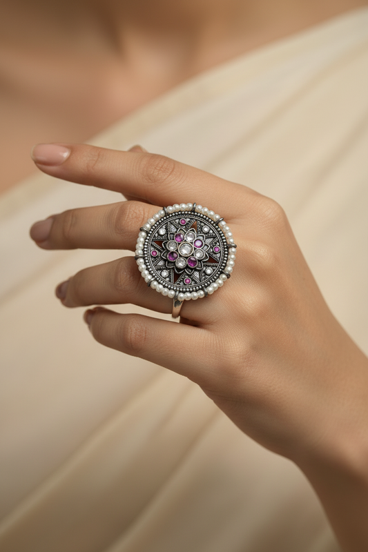 Close-up of a hand wearing a decorative ring with pearls and gemstones on a neutral background