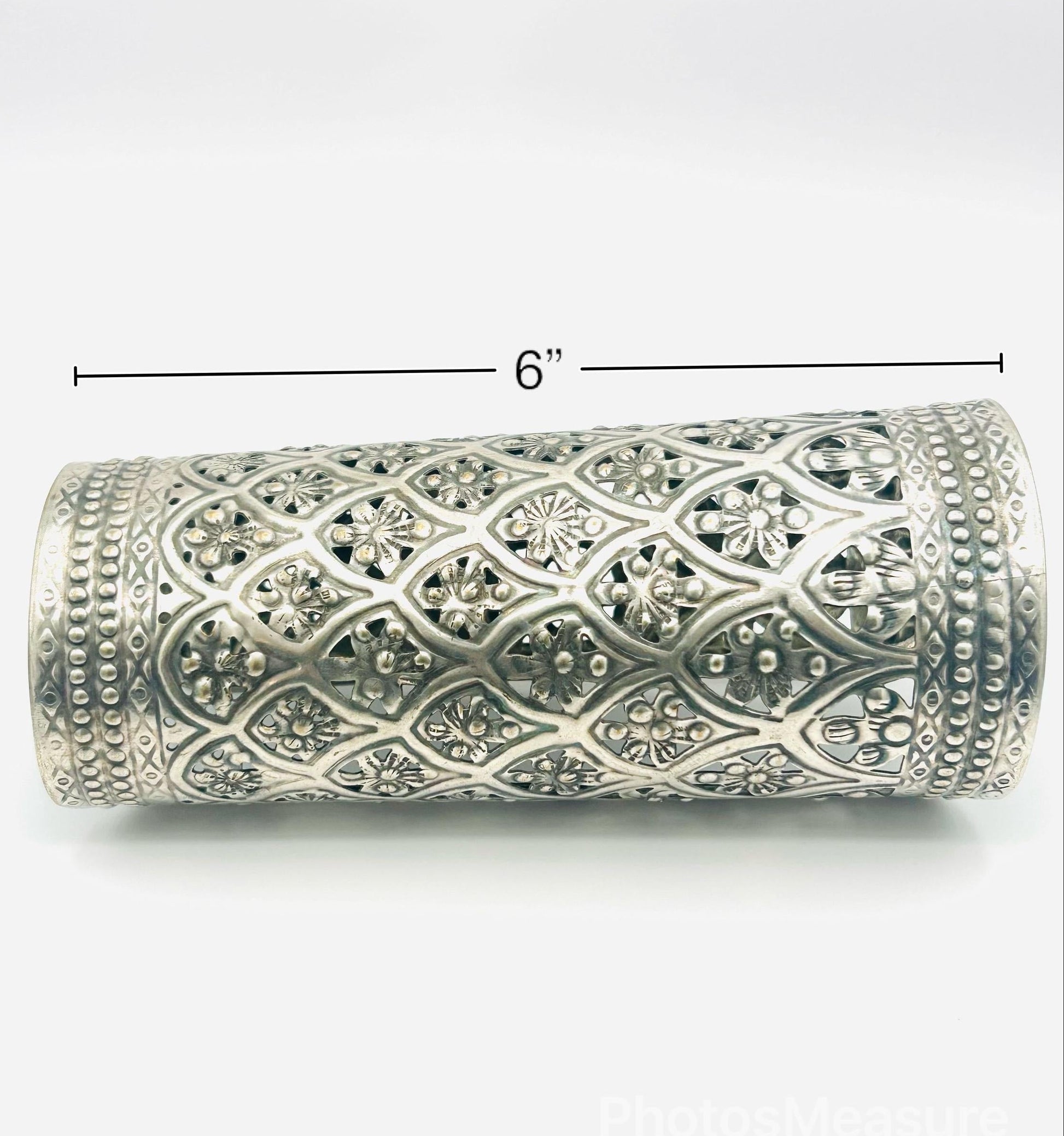Decorative silver cylindrical object with intricate patterns on a white background