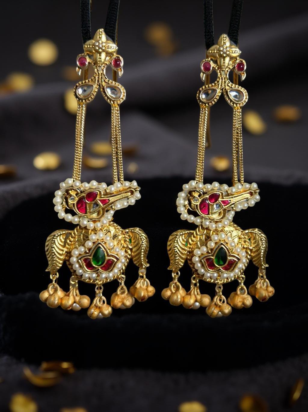 Pair of ornate gold earrings with red and green gemstones on a dark background
