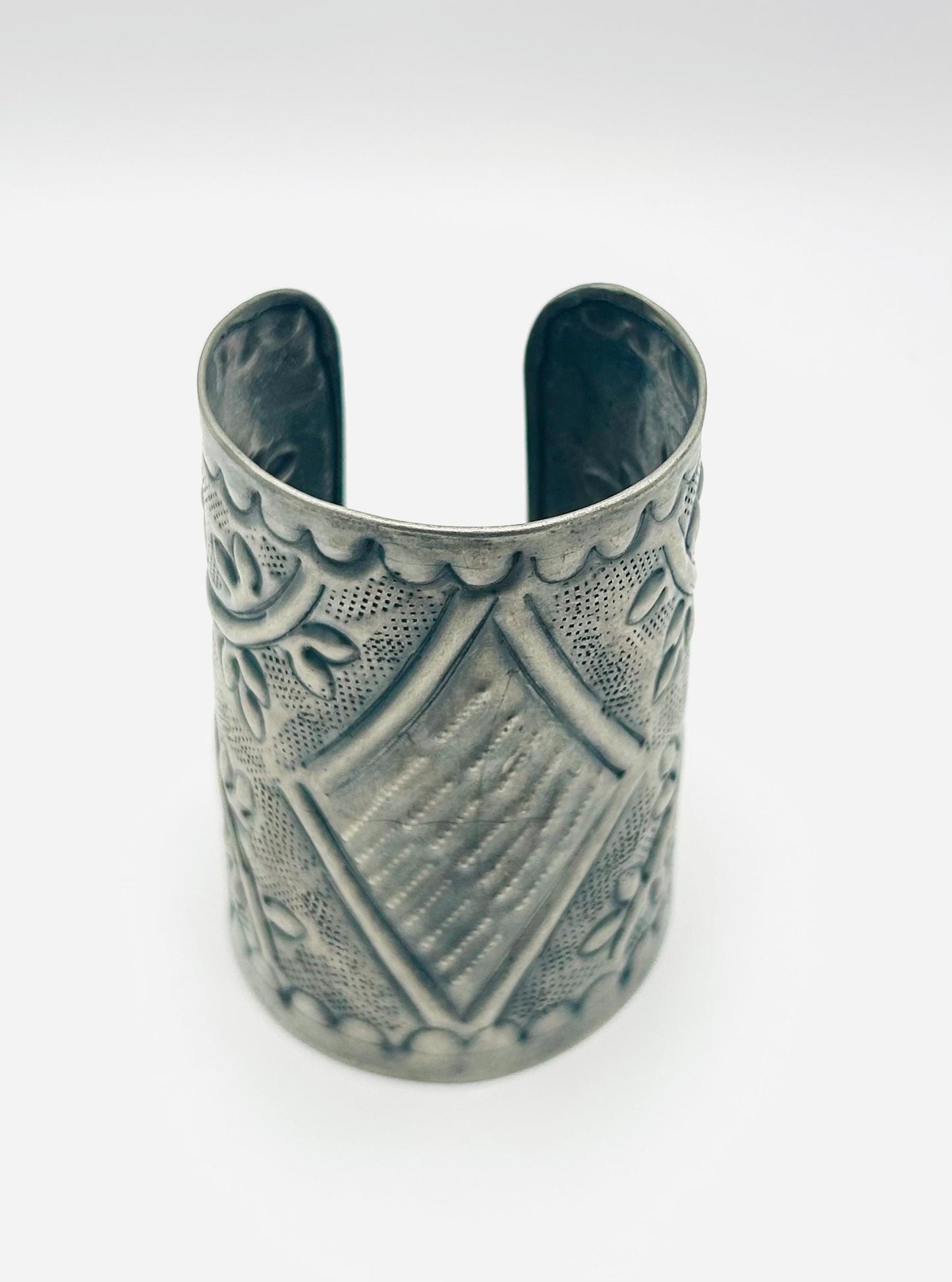 Silver cuff bracelet with intricate patterns on a white background