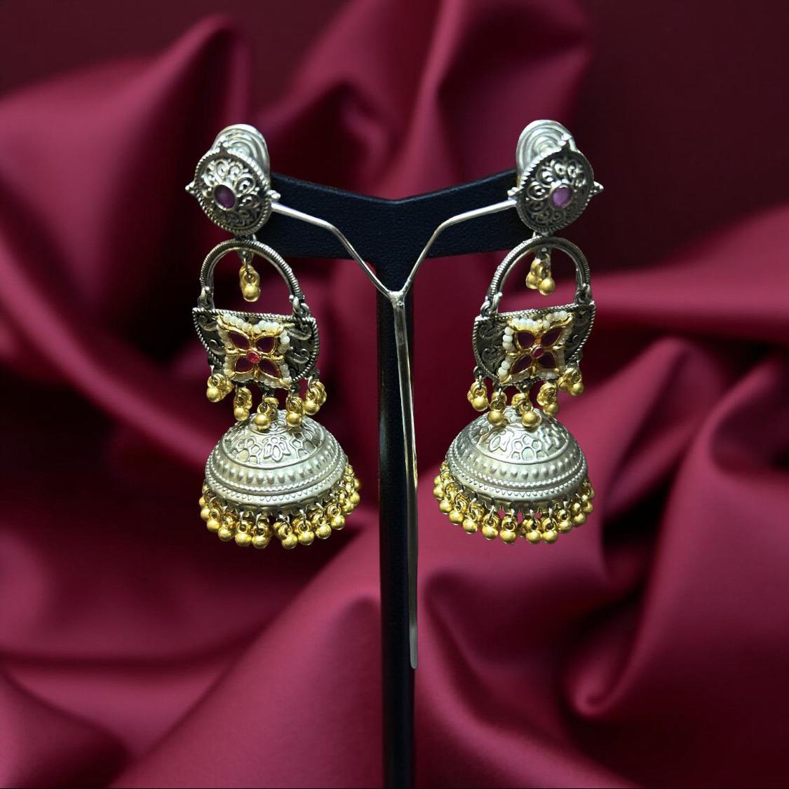 Ornate silver and gold earrings on a stand with a maroon fabric background
