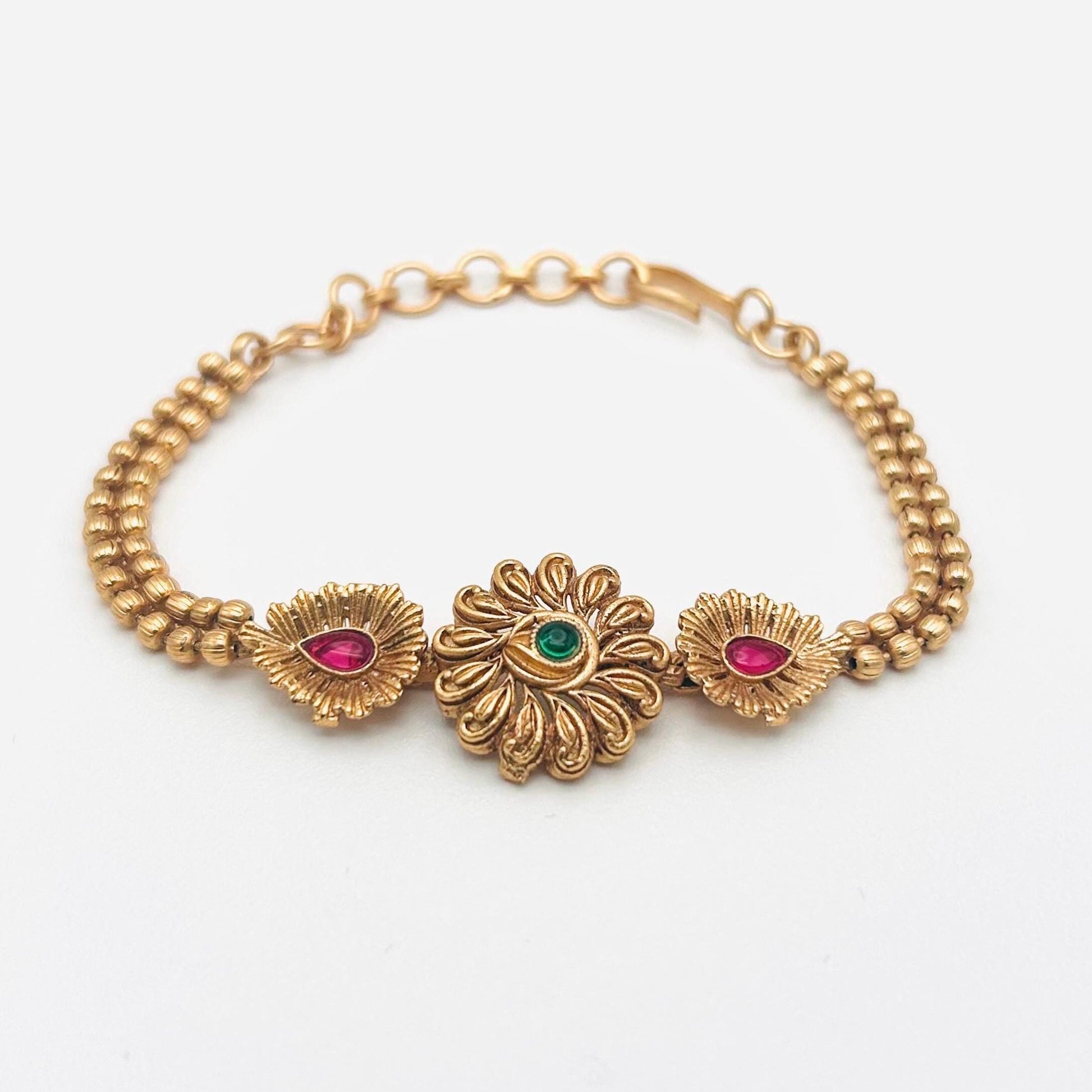 Gold bracelet with floral designs and gemstones on a white background