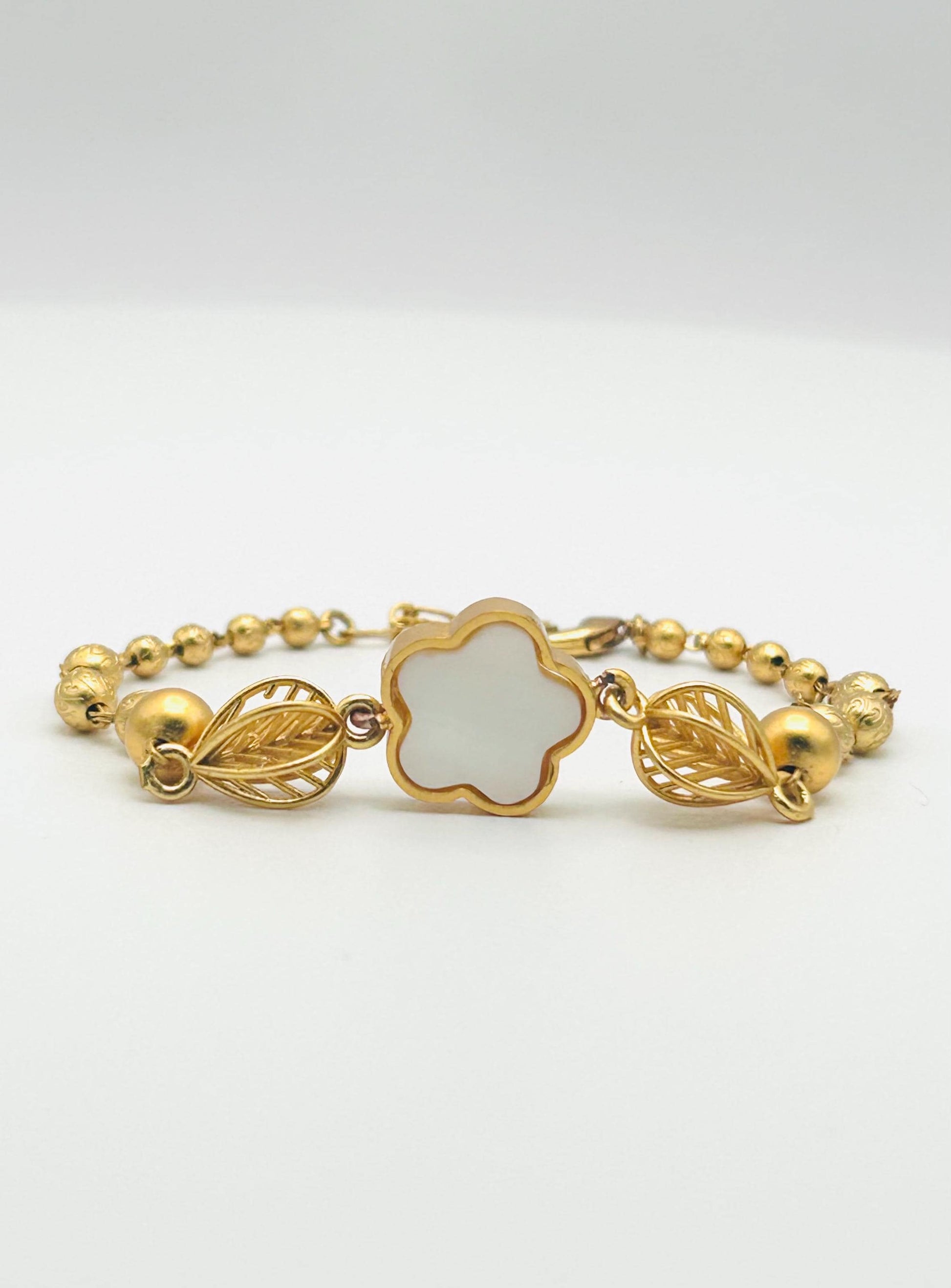 Gold bracelet with a clover-shaped center on a white background