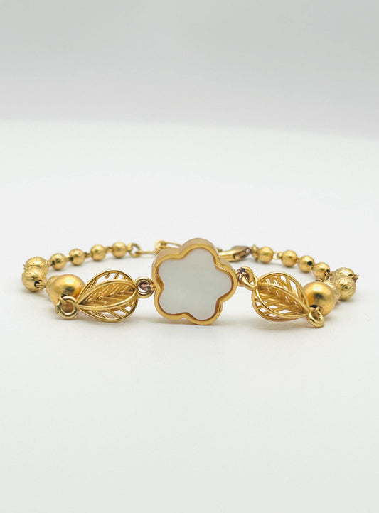 Gold bracelet with a clover-shaped center on a white background
