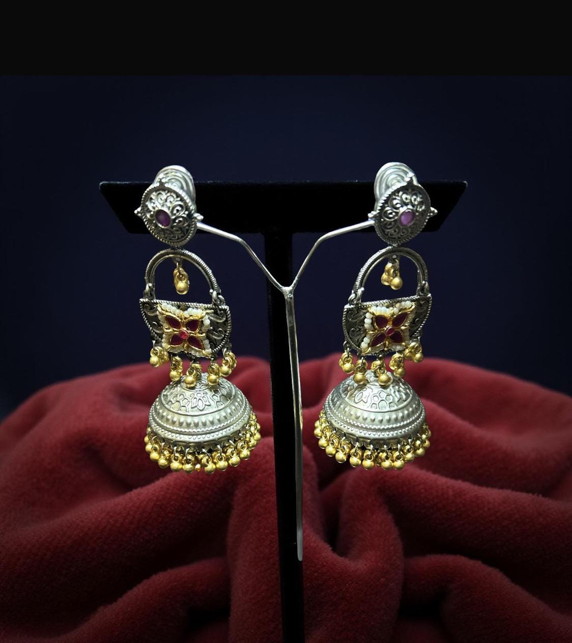 Pair of ornate earrings on a dark stand with a red fabric background