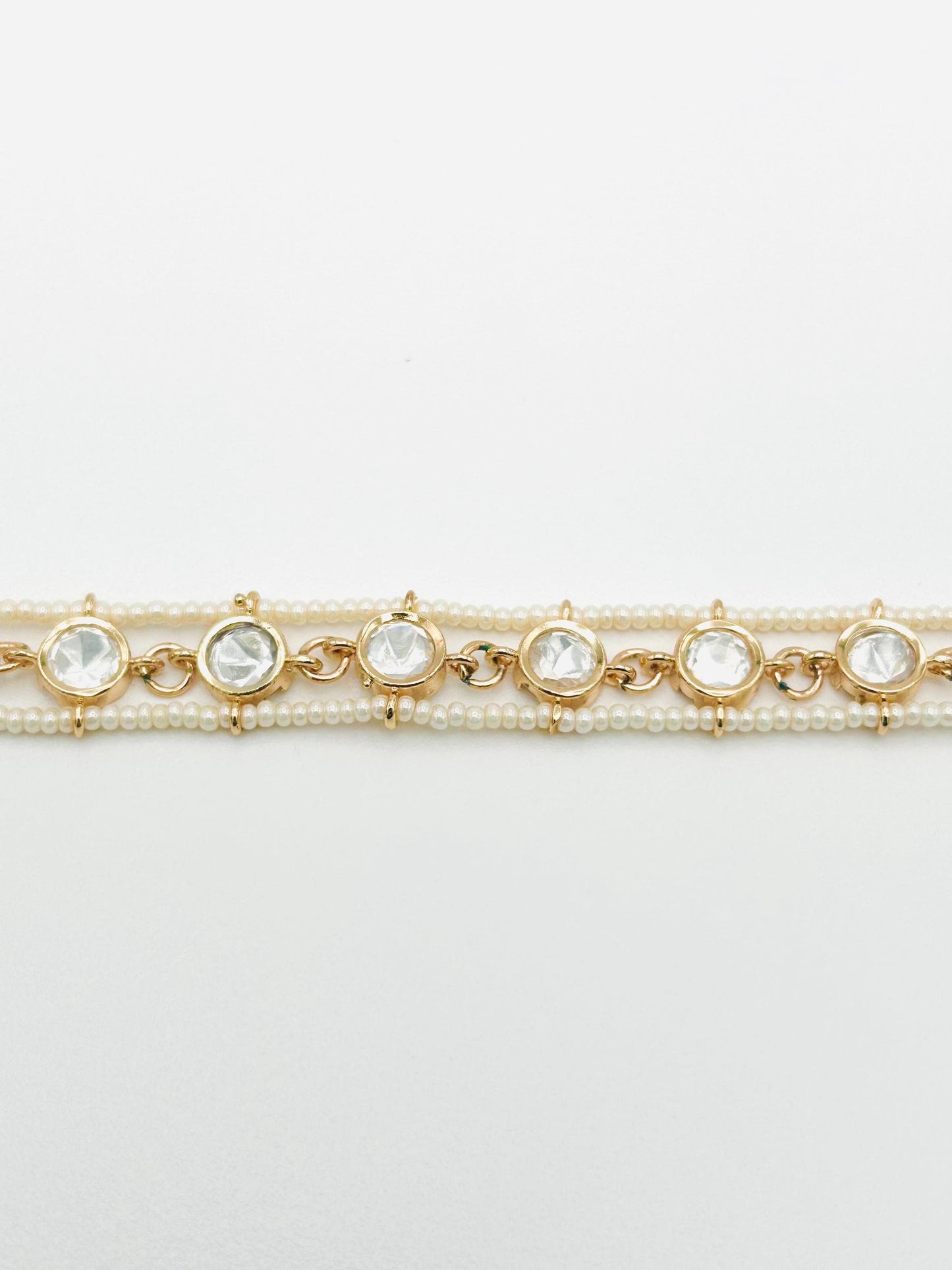 Two gold bracelets with pearl and crystal accents on a light gray background