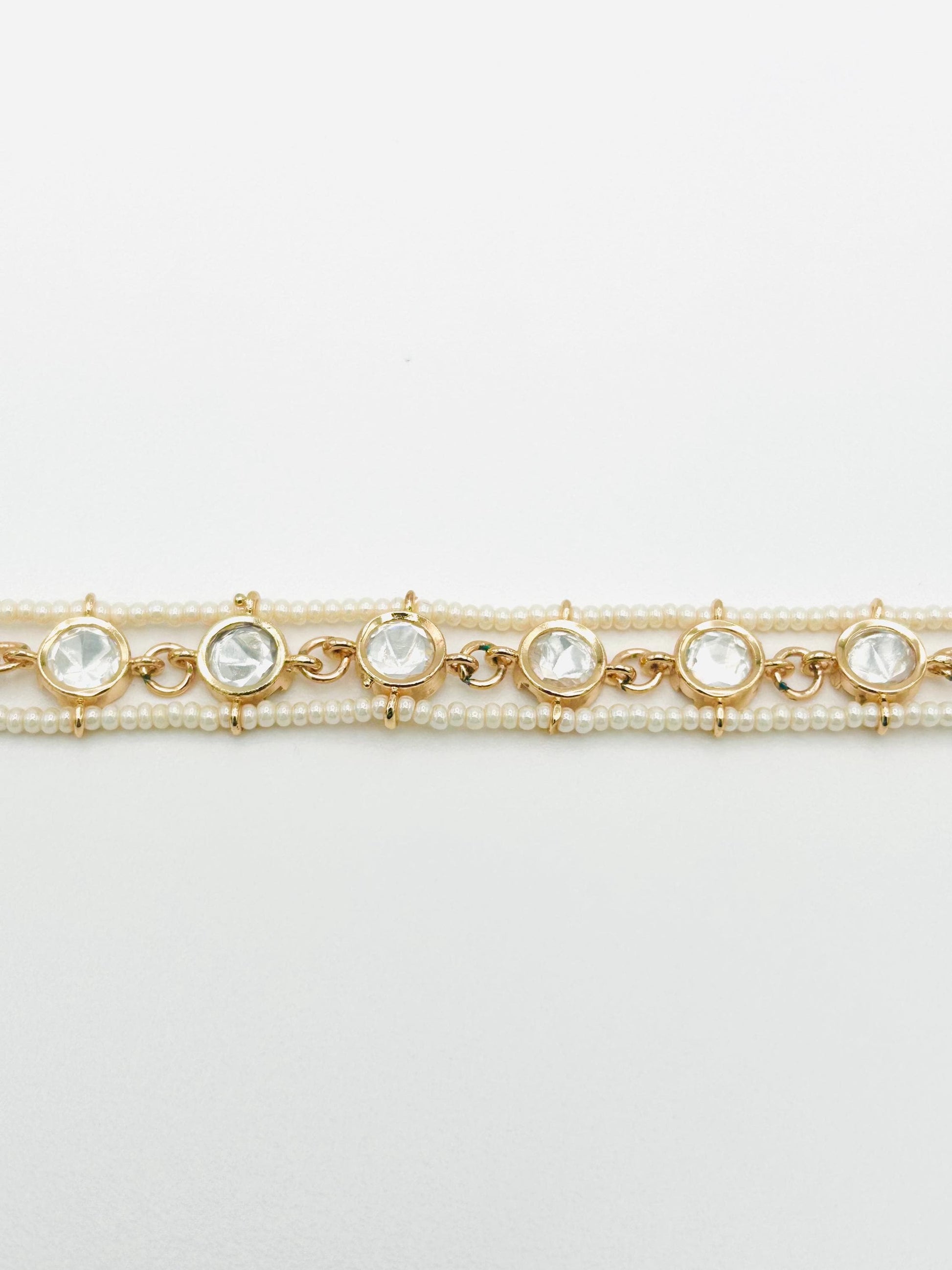 Two gold bracelets with pearl and crystal accents on a light gray background